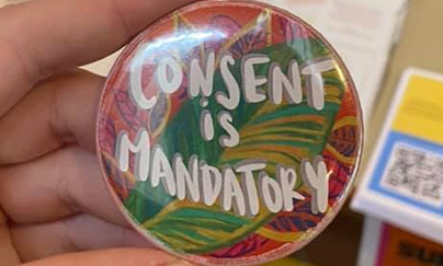 A close-up of a person's hand holding a rounded-shape pin that says 