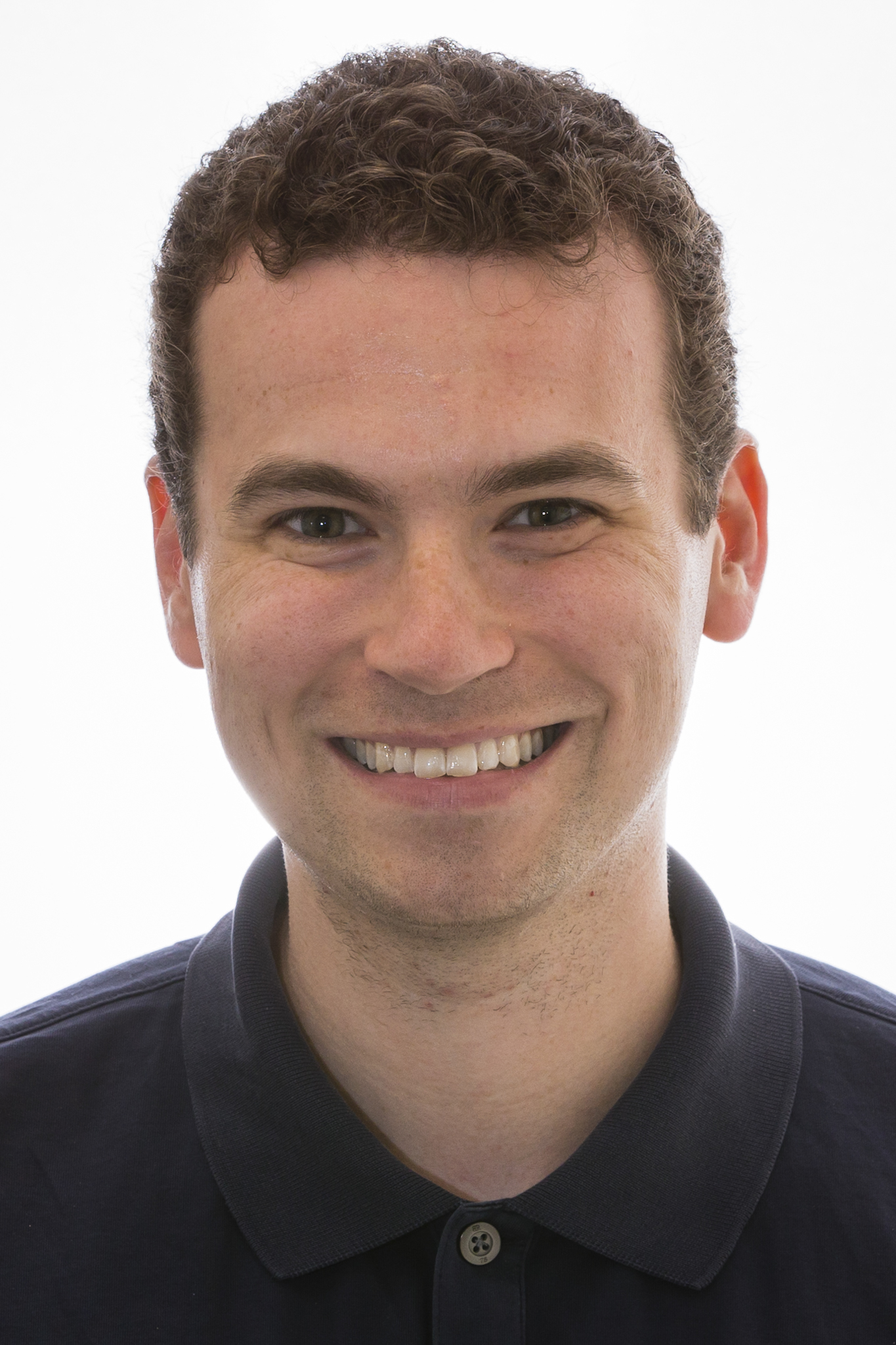 A headshot of smiling Christopher L Asplund who has short brown hair and is wearing a black polo shirt.
