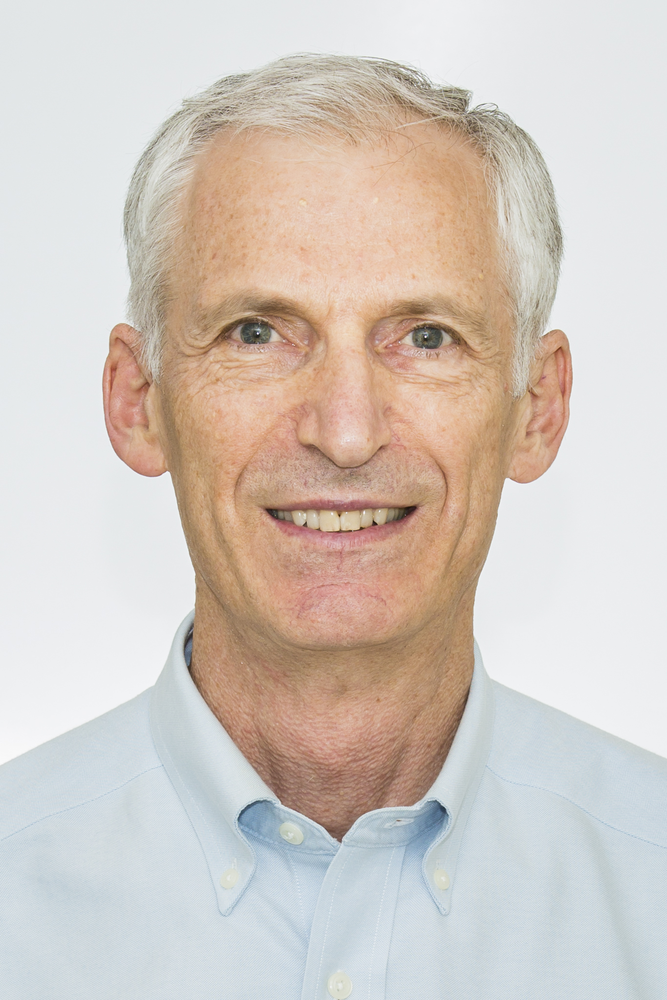 A headshot of smiling A J (Jon) Berrick who has short white hair, wearing a light blue shirt.