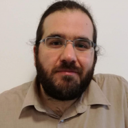 A headshot of smiling Bruno Bodin who has brown hair and a beard, wearing a brown shirt and half-rimmed glasses.