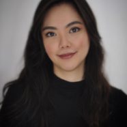A headshot of smiling Christine Abigail Lee Tan who has wavy, long black hair, and is wearing a black turtleneck shirt.