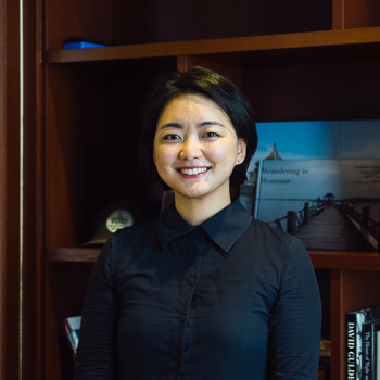A headshot of smiling Chaewon Ahn who has short black hair, wearing a black shirt with bookshelves in the background.