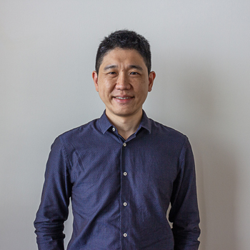 A headshot of smiling Chan Kiat Hwa who has short black hair and is wearing a long-sleeved collared shirt in an indigo shade.